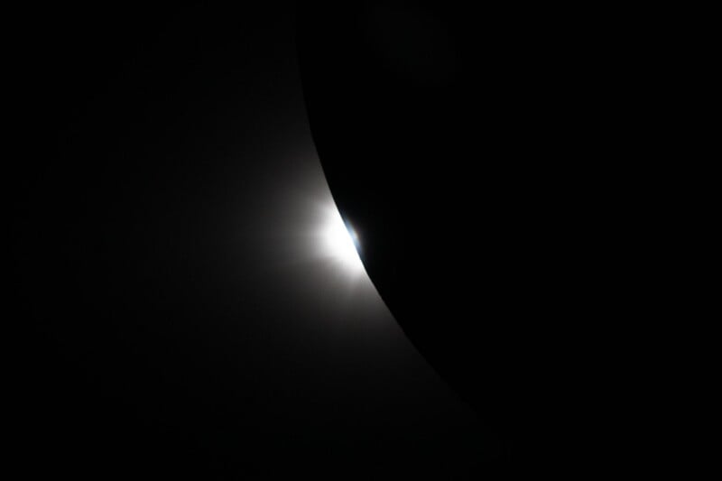 A bright light source partially obscured by a dark, curved object, creating a glowing edge effect against a black background.