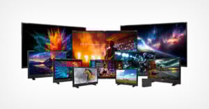 A group of colorful monitors and TVs of various sizes display vibrant images, including nature scenes, people, animals, and abstract designs, all arranged against a plain white background.