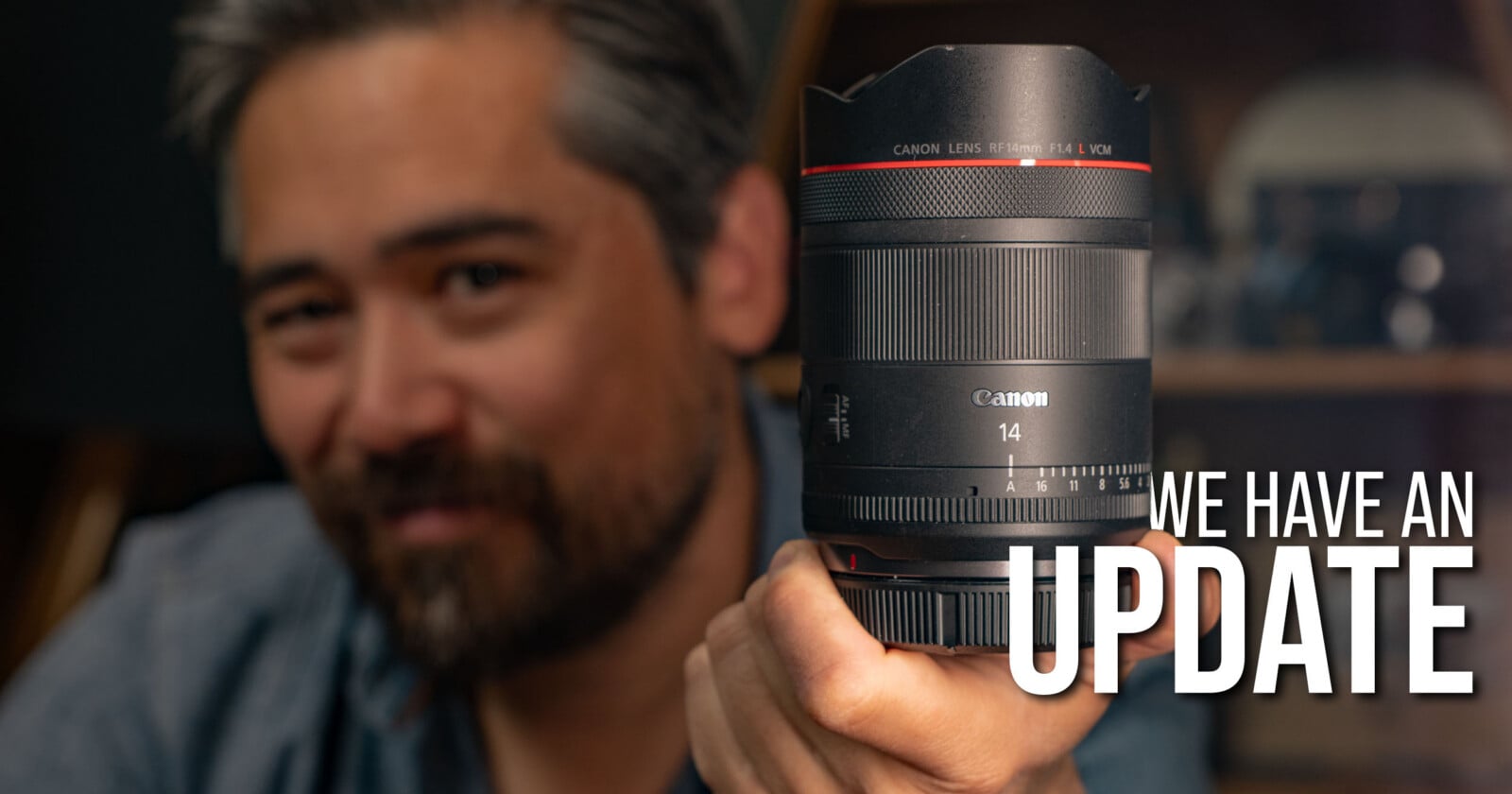 A person with salt-and-pepper hair holds a Canon 14mm camera lens toward the camera. The text "WE HAVE AN UPDATE" appears prominently on the right side of the image.