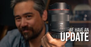 A person with salt-and-pepper hair holds a Canon 14mm camera lens toward the camera. The text "WE HAVE AN UPDATE" appears prominently on the right side of the image.