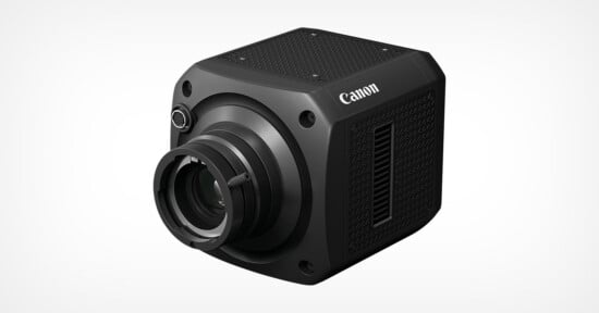 A compact, black Canon camera with a cube-like shape, textured sides, a prominent lens, and the Canon logo on the top right side, set against a plain white background.