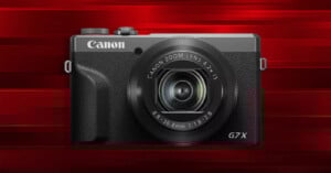 A Canon G7X digital camera with a zoom lens is displayed against a red, striped background.