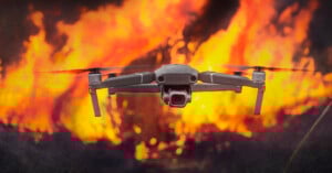 A drone flies in front of large flames and thick smoke, appearing to film or monitor a raging fire in the background.