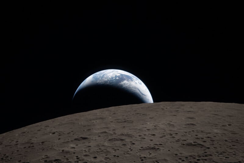 A view of Earth rising above the cratered, gray surface of the Moon against the blackness of space.