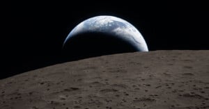 A view of Earth rising above the Moon’s cratered surface, showing a curved horizon and Earth's blue and white colors against the blackness of space.