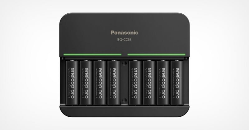 A Panasonic battery charger, model BQ-CC63, is charging eight Eneloop Pro AA rechargeable batteries, with a green light strip indicating charging status.