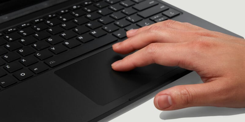 A close-up of a person's right hand using the touchpad on a black laptop keyboard.
