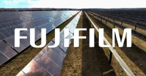 Rows of solar panels in a large field under a bright sky, with the word "FUJIFILM" in bold white letters overlaid across the center of the image.