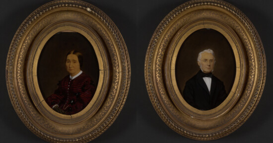 Two oval-framed painted portraits: on the left, a woman in a dark red dress with a patterned design; on the right, a man in a dark suit with a bow tie. Both portraits are set against dark backgrounds.