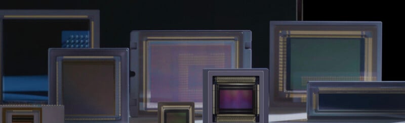Several rectangular image sensors of varying sizes are displayed upright in front of a dark background, showcasing their reflective surfaces and intricate internal circuitry.