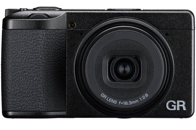 A black compact digital camera with a prominent lens, textured grip on the left, and "GR" branding in white letters on the bottom right corner of the front panel.