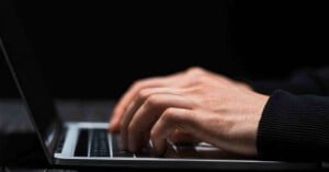 A close-up of hands typing on a laptop keyboard against a dark background.