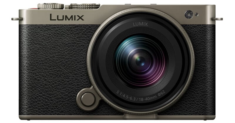 Front view of a Panasonic LUMIX digital camera with a black textured grip, large round lens, and metallic accents. The camera displays the brand name "LUMIX" above the lens.