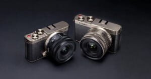 Two silver Panasonic Lumix digital cameras with black textured grips and attached wide-angle lenses are placed side by side on a dark surface.