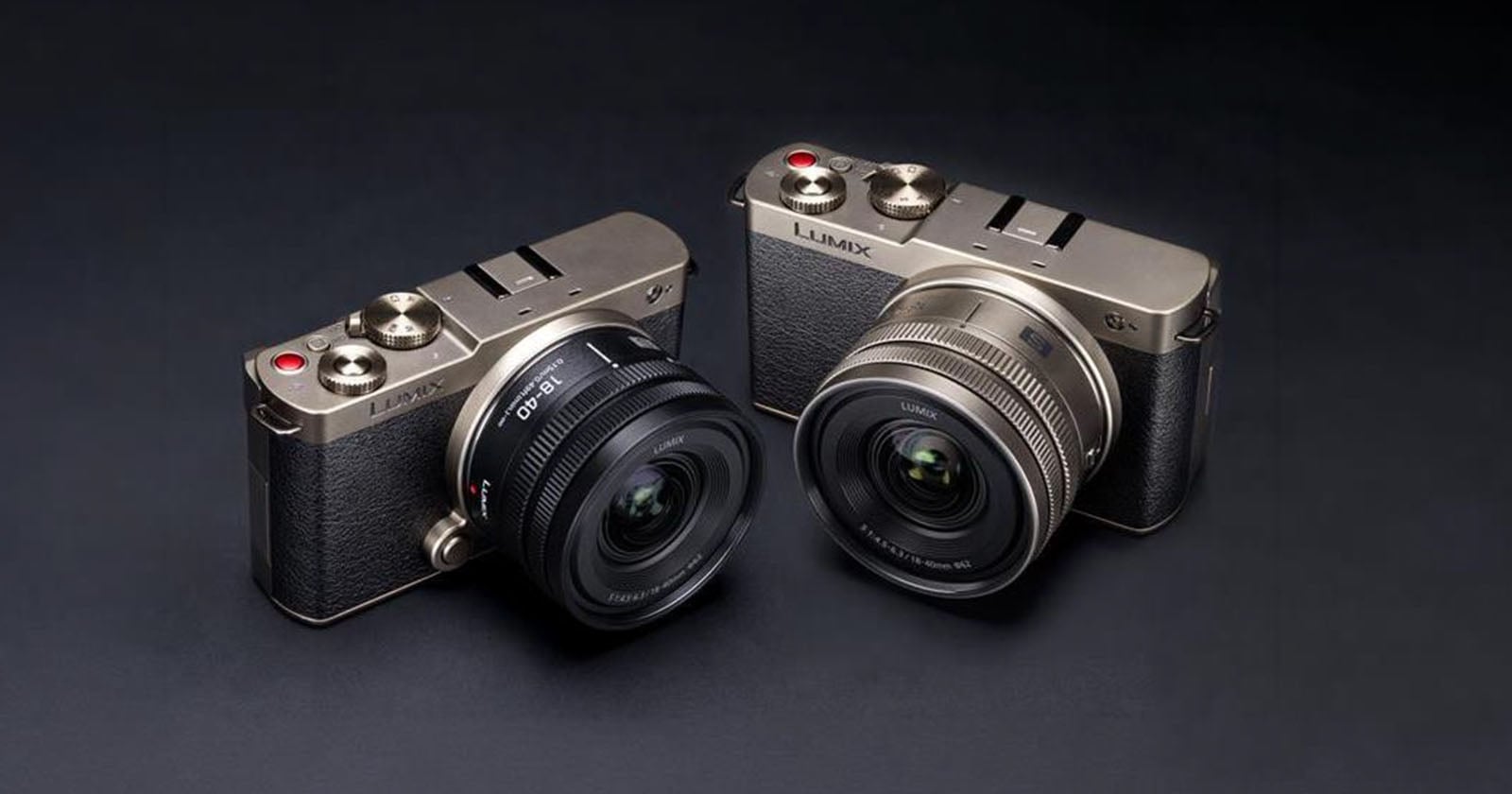 Two silver Panasonic Lumix digital cameras with black textured grips and attached wide-angle lenses are placed side by side on a dark surface.