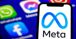 A smartphone displays the Meta logo and text, with blurred icons of WhatsApp, Messenger, Facebook, and Instagram visible on a screen in the background.