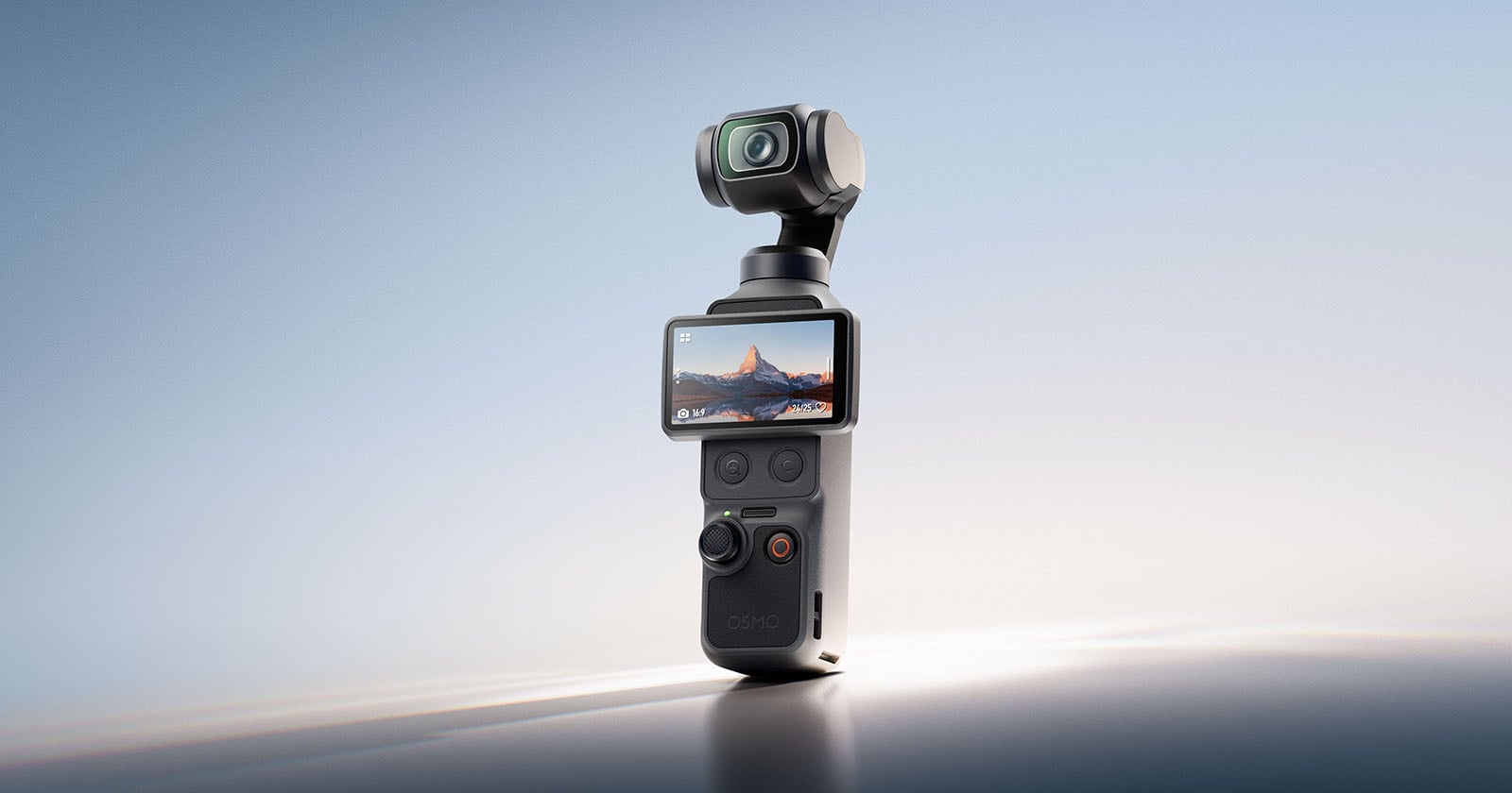 A compact handheld camera with a built-in gimbal stands upright. Its screen displays a landscape with mountains at sunset. The device has several buttons and a joystick on the front. The background is softly lit and minimalistic.