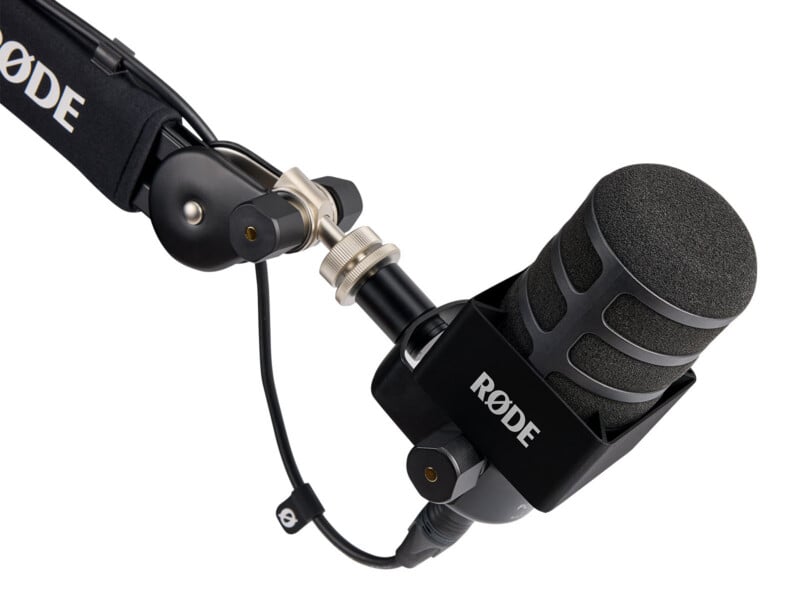 A close-up of a black RØDE microphone mounted on an adjustable boom arm, viewed against a white background.
