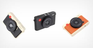 Three compact cameras are displayed on a white background: one cream with black accents, one all black, and one cream with orange and black accents. Each has a lens with visible writing on it.