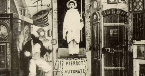A vintage black-and-white image shows a mechanical man in white costume standing in a box labeled "Pierrot Automate," surrounded by gears and strange machinery, while another person moves energetically beside the box.