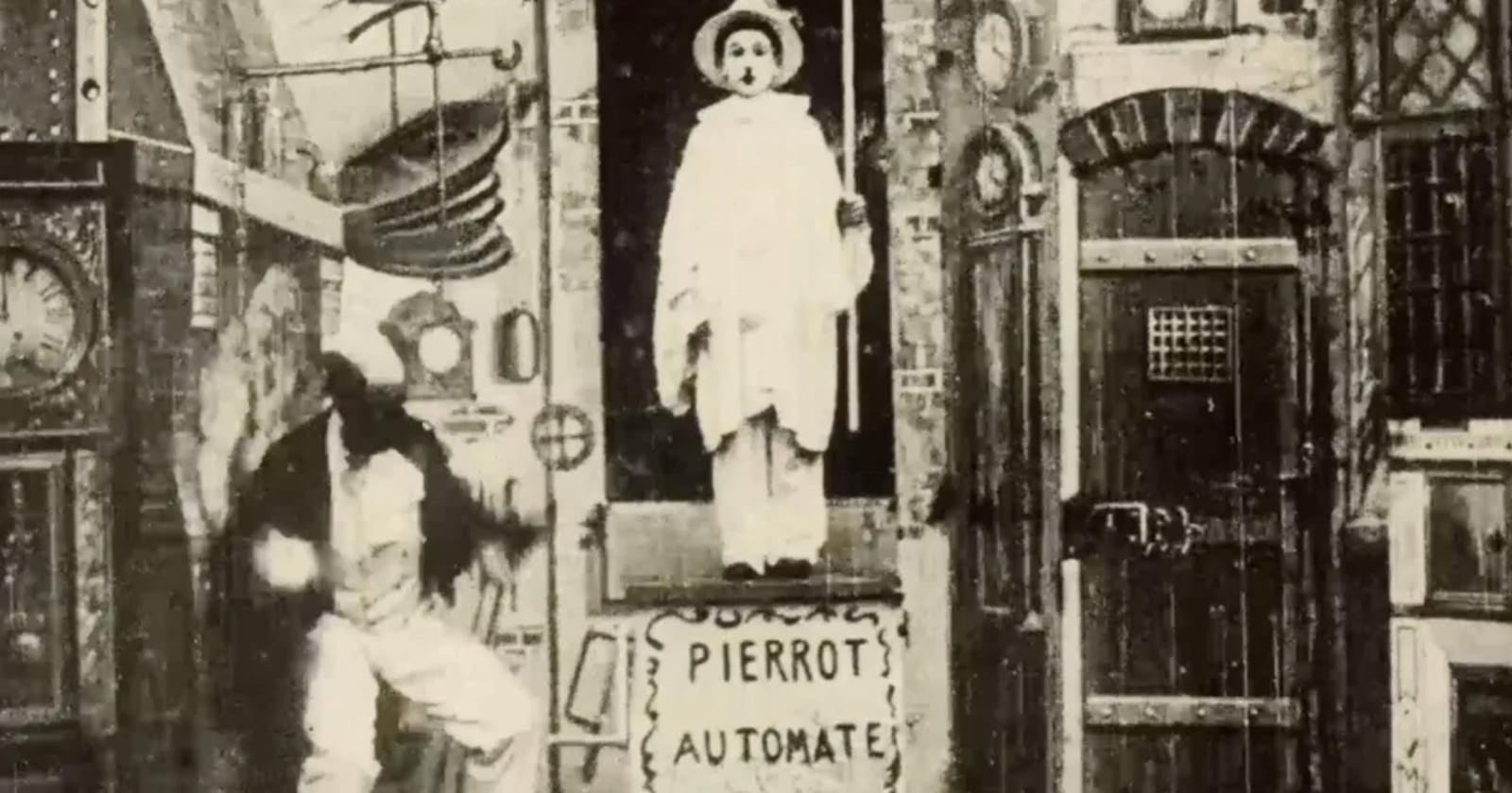 A vintage black-and-white image shows a mechanical man in white costume standing in a box labeled "Pierrot Automate," surrounded by gears and strange machinery, while another person moves energetically beside the box.
