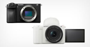 Two Sony Alpha series mirrorless cameras: the black one with no lens attached (top) and the white one with a lens and flip-out screen facing forward (bottom), both on a plain white background.