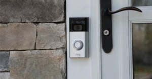 A Ring video doorbell is mounted next to a white door with a black handle, attached to a stone wall.