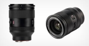 Two black camera lenses are shown against a white background. The lens on the left is upright, while the lens on the right is angled with its front glass and markings visible. Both lenses have textured focus rings.