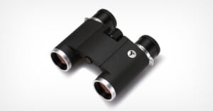 A pair of compact black binoculars with silver accents, viewed at an angle from above, against a white background.