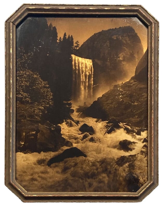 Sepia-toned framed photograph of a powerful waterfall cascading down rocky cliffs, surrounded by trees and mist, with turbulent water flowing in the foreground.