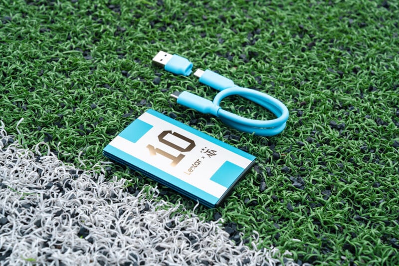 A blue and white portable Lexar device with the number 10 on it and a matching short USB cable on artificial grass near a white line.