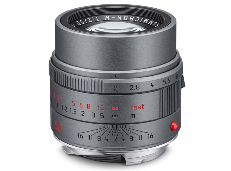 A silver camera lens with engraved focus and aperture markings in red, white, and black, labeled "SUMMICRON-M 1:2/50" on the front, resting upright on a white background.