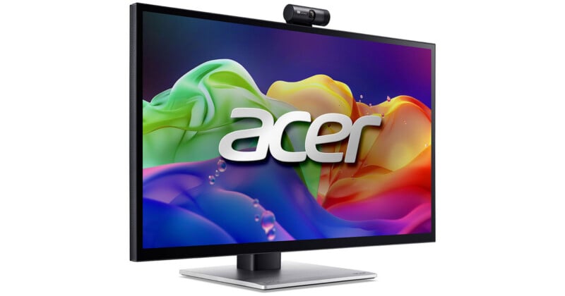 A computer monitor displaying a colorful abstract background with the Acer logo in the center. The monitor has a built-in webcam on top and sits on a silver stand.
