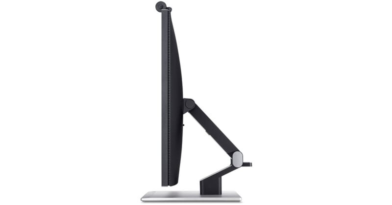 Side view of a modern flat-screen computer monitor on an adjustable stand, showing its slim profile and flexible arm, positioned on a rectangular base against a white background.