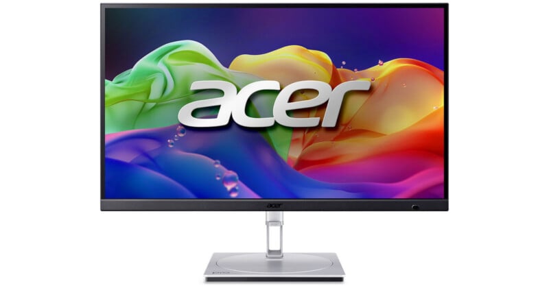 A sleek Acer computer monitor displays a vibrant, colorful abstract background with the Acer logo in the center. The monitor has thin bezels and a sturdy silver stand.