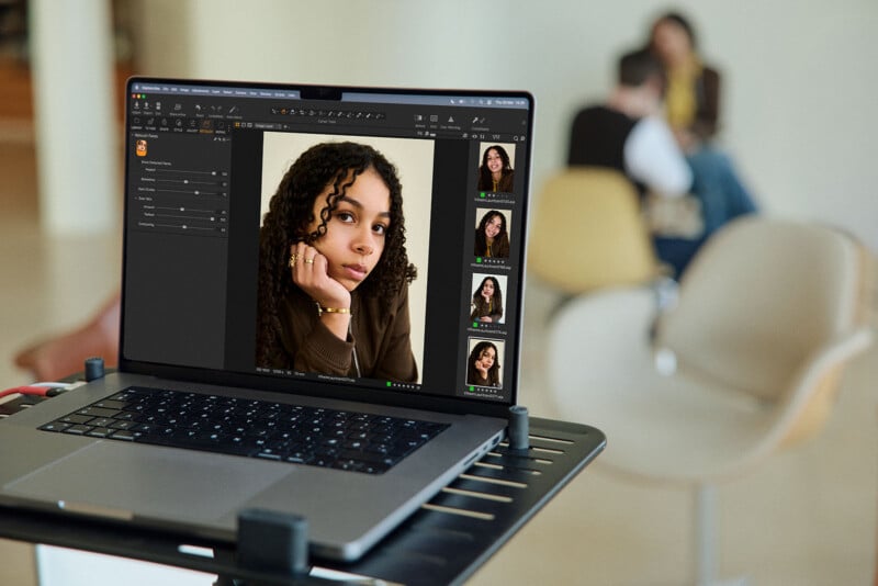 A laptop on a table displays portrait photos of a woman in photo editing software, with a blurred background showing people sitting and talking in a modern indoor space.