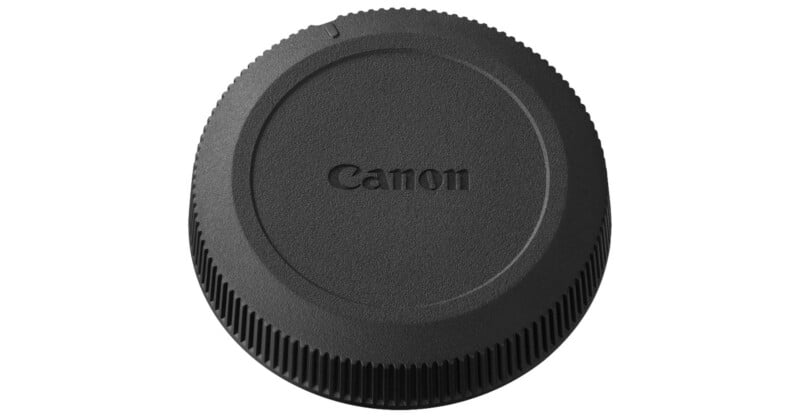 A black Canon camera lens cap seen from above, featuring the Canon logo embossed in the center, with ridged edges for grip.