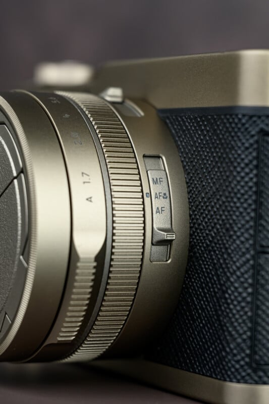 Close-up of a camera lens showing a textured grip and a focus mode switch with three options labeled MF, AFS, and AF. The camera body features a dark textured surface and metallic finish.