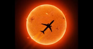 A silhouette of an airplane flies directly in front of the glowing orange Sun, showing solar details like flares and sunspots against the bright background.