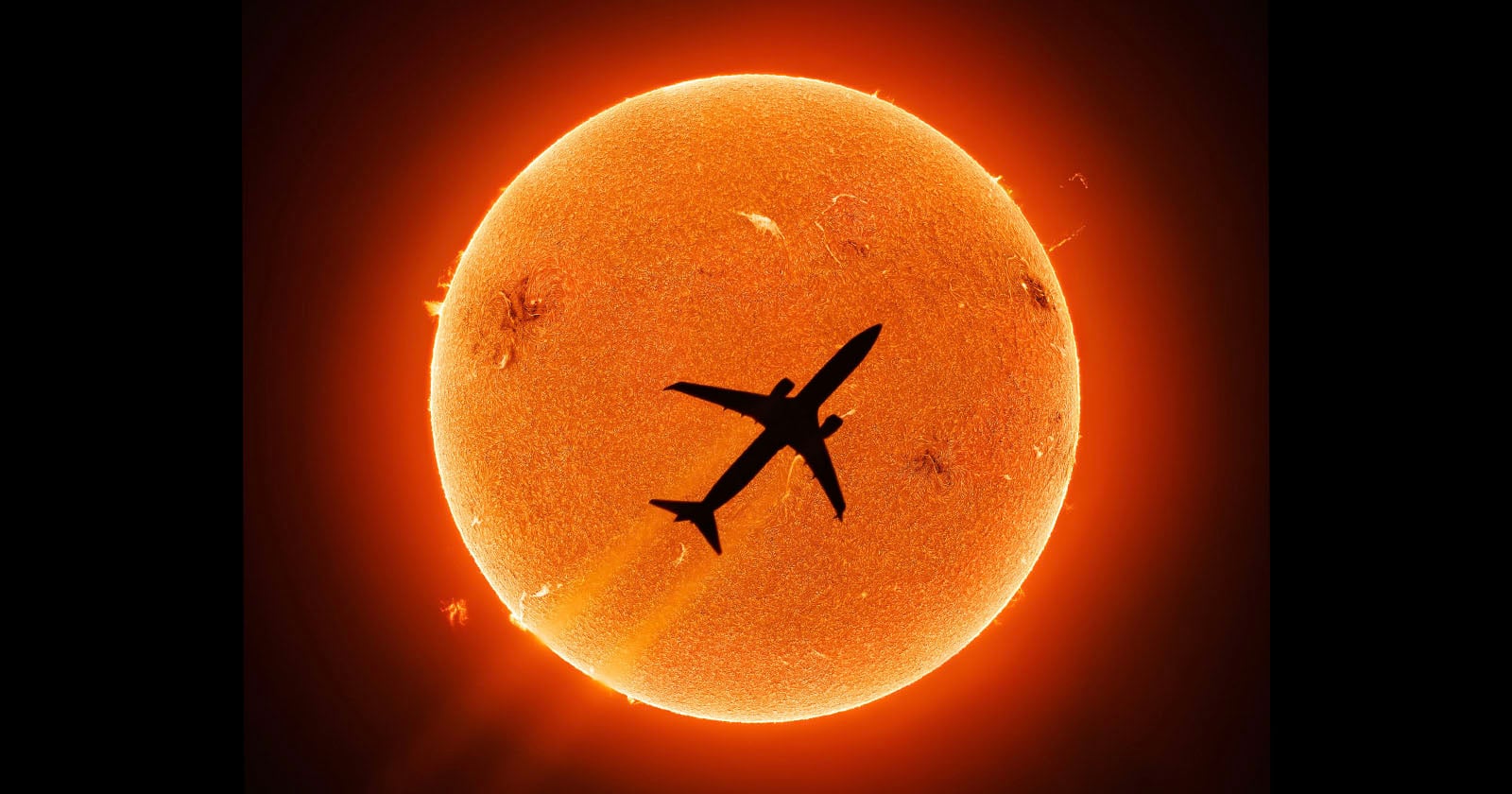 A silhouette of an airplane flies directly in front of the glowing orange Sun, showing solar details like flares and sunspots against the bright background.