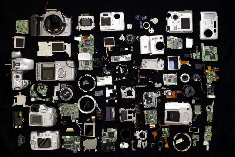 A collection of dismantled digital cameras and their internal components arranged neatly on a black background, showcasing circuit boards, lenses, casings, screens, and various small parts.