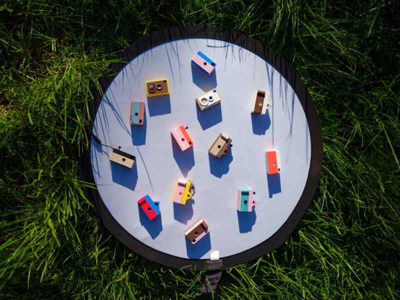 A circular white mat placed on grass holds several small, colorful toy blocks scattered across its surface in sunlight.