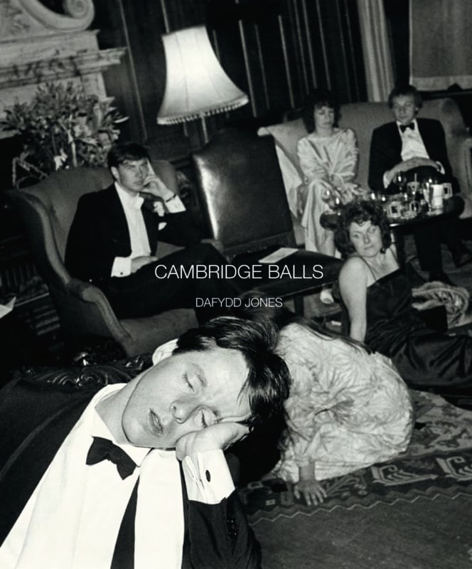 A black-and-white photo of people in formal attire at a party. One man in the foreground is asleep with his head resting on his hand. Others sit or lounge on chairs and the floor, looking tired or relaxed. Text reads “CAMBRIDGE BALLS DAFYDD JONES.”.