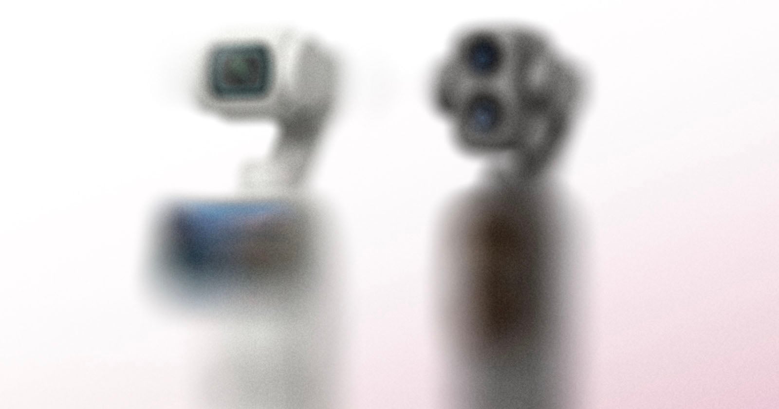 Two small robotic camera devices are shown side by side against a soft, pinkish-white background. The image is heavily blurred, making the objects indistinct and lacking clear detail.