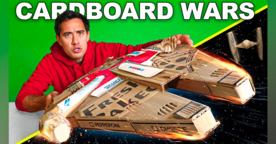 A man in a red hoodie holds a cardboard spaceship made from pizza boxes, styled like the Millennium Falcon. The background is split between green and a space scene with a small TIE fighter. Text reads "CARDBOARD WARS.
