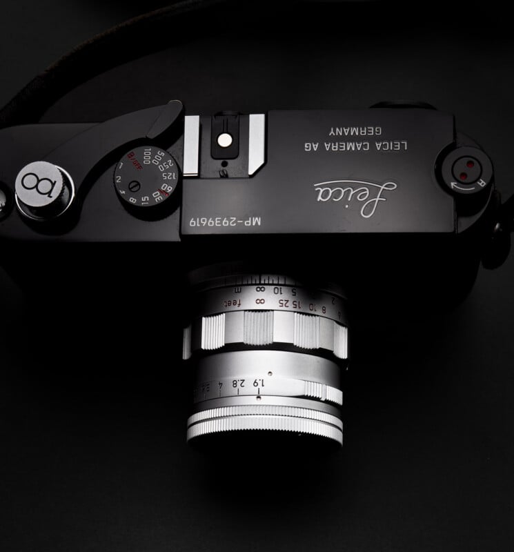 A close-up, top view of a black Leica camera with a silver lens against a dark background. The camera’s dials, brand logo, and serial number are clearly visible.