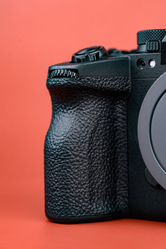Close-up of the textured grip and control dials on a black digital camera body against a solid orange background.