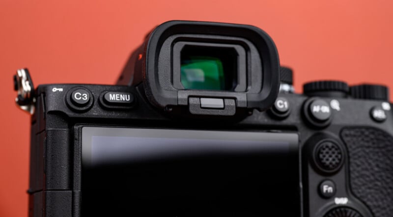 Close-up of the back of a digital camera, focusing on the electronic viewfinder, buttons (including C3, Menu, and Fn), and part of the LCD screen, with an orange background.