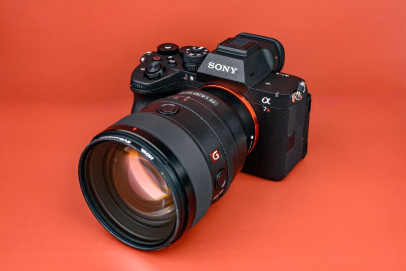 A Sony Alpha 7R mirrorless digital camera with a large zoom lens attached, displayed against a solid orange background.