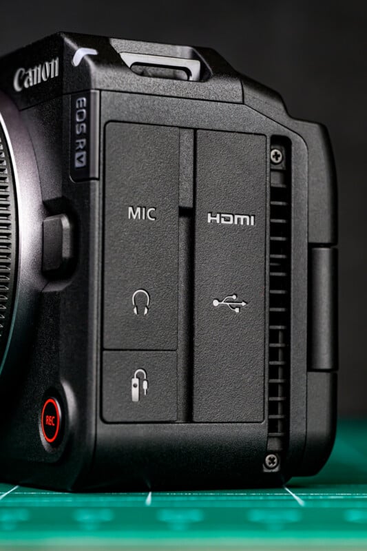 Close-up of the side of a Canon EOS R7 camera showing labels for MIC, HDMI, and USB ports, with a REC button and headphone symbol visible near the bottom on a green surface.